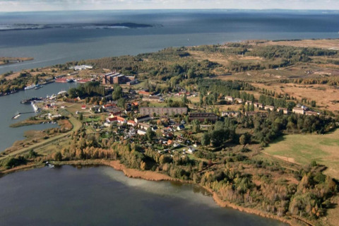 Luchtfoto van een woonboot in Peenemünde, Duitsland, met water, groen en enkele gebouwen.