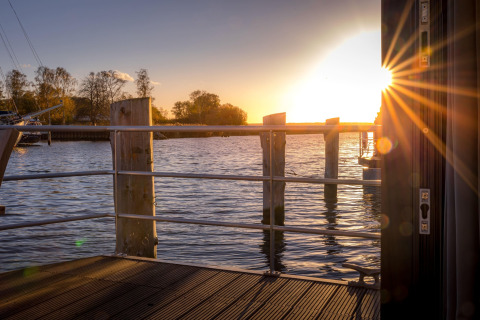 Zonsondergang vanaf een woonboot in Peenemünde met zicht op het water, houten dek en leuning.