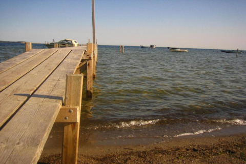 Molo di legno che si estende sull'acqua presso Houseboat a Peenemünde, con barche e cielo sereno.