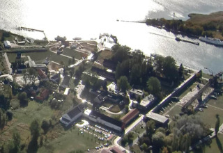 Aerial view of a houseboat in Peenemünde, surrounded by greenery, buildings, and shimmering water.