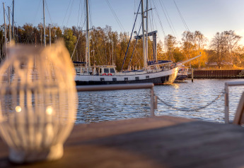 Blick von einem Hausboot in Peenemünde auf ein Segelboot am Steg bei Sonnenuntergang.
