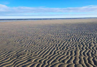 Plage de sable aux motifs ondulés, vue depuis Houseboat à Peenemünde, sous un ciel bleu et des nuages.