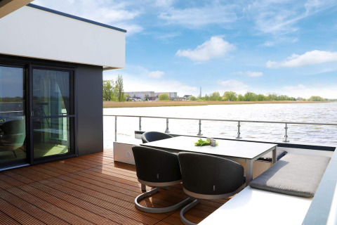 Modern terrace overlooking water on houseboat in Ribnitz-Damgarten, Germany, featuring outdoor seating.