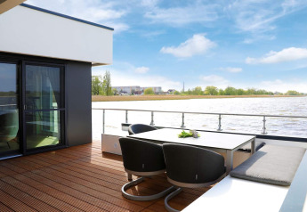Moderne terrasse med udsigt til vandet på husbåd i Ribnitz-Damgarten, Tyskland, med havemøbler.