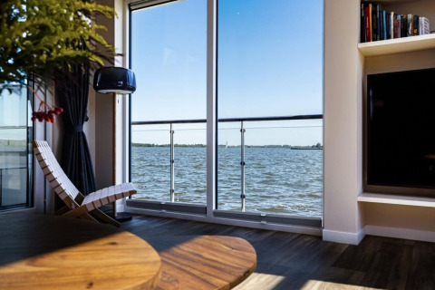 Soggiorno su una houseboat a Ribnitz-Damgarten, Germania, con vista sull’acqua attraverso ampie finestre.