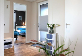 Lichte en moderne inkomhal van een woonboot in Ribnitz-Damgarten, Duitsland, met bloemen en zicht op slaapkamer.