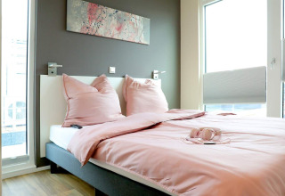 Camera da letto su una houseboat a Ribnitz-Damgarten, Germania, con biancheria rosa e finestre luminose.