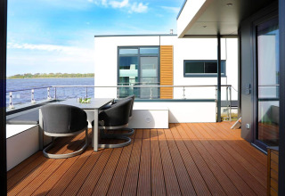 Terraza de casa flotante moderna con mesa y sillas junto al agua en Ribnitz-Damgarten, Alemania.