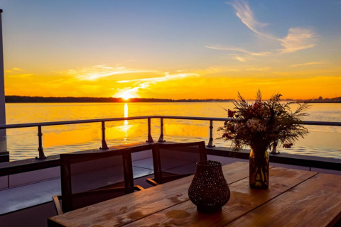 Zonsondergang vanaf een woonboot in Ribnitz-Damgarten, Duitsland, met bloemen en zicht op het water.