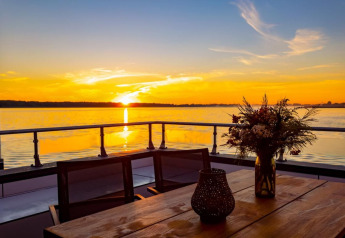 Vue du coucher de soleil depuis une péniche à Ribnitz-Damgarten, Allemagne, avec table et fleurs.