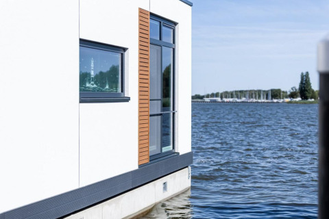 Casa flotante moderna en Ribnitz-Damgarten, Alemania, con grandes ventanas y vistas al agua y puerto.