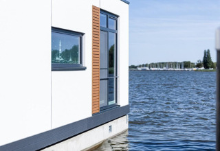 Moderne woonboot in Ribnitz-Damgarten, Duitsland, met grote ramen en zicht op het water en de jachthaven.