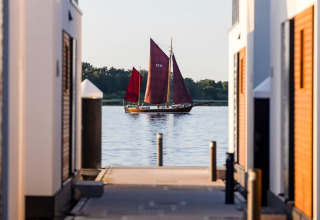 Barca a vela con vele rosse tra le case galleggianti sull'acqua a Ribnitz-Damgarten, in Germania.