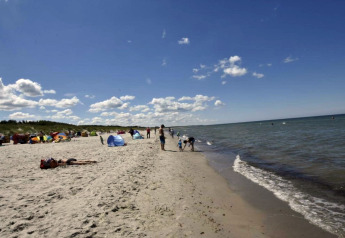 Sonniger Strand mit Badegästen und Zelten nahe dem Hausboot in Ribnitz-Damgarten, Deutschland.