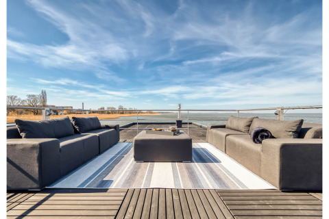 Moderne husbådterrasse i Ribnitz-Damgarten med komfortable sofaer, et sofabord og flot udsigt over vandet.