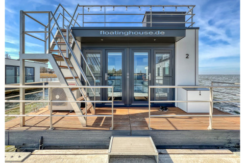 Moderne husbåd ved vandkanten i Ribnitz-Damgarten med terrasse, glasdøre og udendørs trappe.