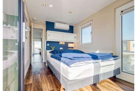 Moderne slaapkamer op een woonboot in Ribnitz-Damgarten met blauwe details en zicht op het water.