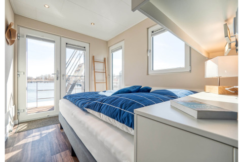 Lichte slaapkamer op een woonboot in Ribnitz-Damgarten met grote ramen en zicht op het water.