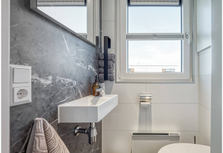 Modern bathroom on a houseboat in Ribnitz-Damgarten with a sink, mirror, window, and gray marble wall.