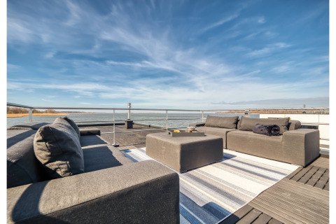 Outdoor lounge on a houseboat in Ribnitz-Damgarten with modern sofas, ottoman, rug, and water view.