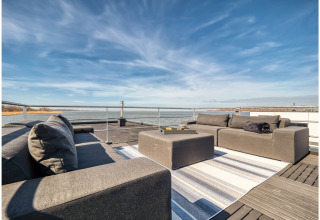 Outdoor lounge on a houseboat in Ribnitz-Damgarten with modern sofas, ottoman, rug, and water view.