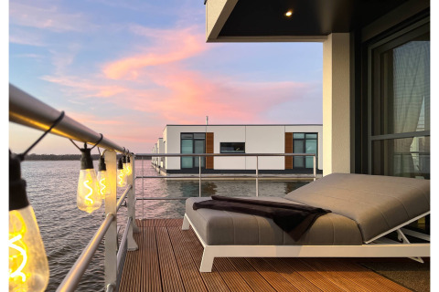 Moderne woonboot-terras met sfeervolle lampjes, ligbed en uitzicht op het water bij zonsondergang in Ribnitz-Damgarten.