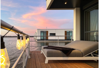 Modern houseboat terrace with chic string lights, a lounge chair, and calm waters at sunset in Ribnitz-Damgarten.