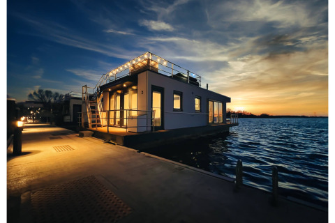 Husbåd i Ribnitz-Damgarten ved solnedgang, oplyst med lys på kajen og roligt vand omkring.