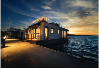 Houseboat in Ribnitz-Damgarten at sunset, warmly lit by pier lights with peaceful water surrounding.