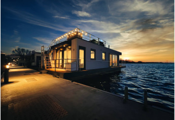 Woonboot in Ribnitz-Damgarten bij zonsondergang, warm verlicht en omringd door kalm water.