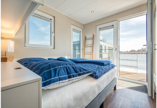 Bedroom with blue bedding on houseboat in Ribnitz-Damgarten, open doors leading to water view balcony.