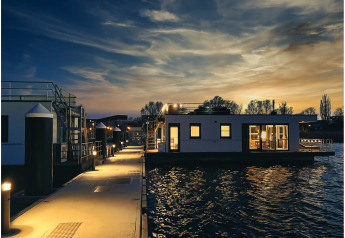 Verlichte woonboot op het water bij zonsondergang in Ribnitz-Damgarten, rustgevende avondscène.