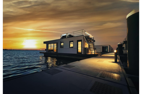 Coucher de soleil sur l'eau à Houseboat à Ribnitz-Damgarten, avec une péniche moderne et une passerelle éclairée.