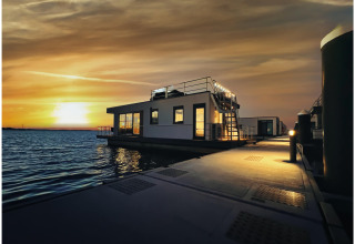 Coucher de soleil sur l'eau à Houseboat à Ribnitz-Damgarten, avec une péniche moderne et une passerelle éclairée.
