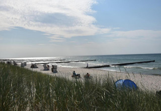 View of a sandy beach with dunes, beach chairs, and people by the sea, taken from a houseboat in Ribnitz-Damgarten.