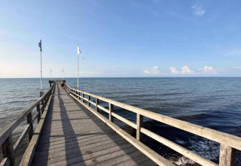Foto van een houten pier met vlaggen die uitsteekt in de rustige zee onder een heldere lucht bij Ribnitz-Damgarten.