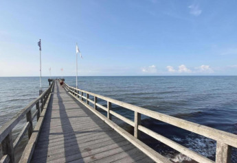 Photo d'une longue jetée en bois ornée de drapeaux s'avançant vers la mer calme à Ribnitz-Damgarten.
