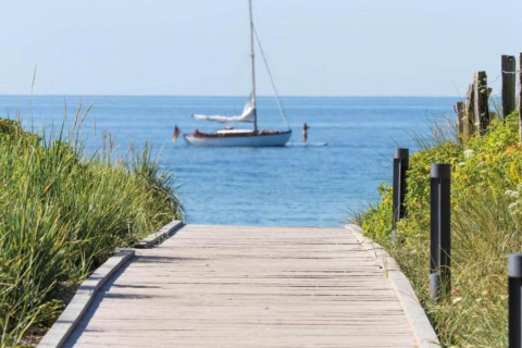 Houten wandelpad naar strand met zicht op een zeilboot bij Houseboat in Ribnitz-Damgarten, Duitsland.