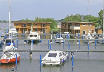 Foto van woonboten en zeilboten in een haven, met moderne houten huizen langs het water op de achtergrond.