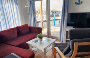 Sala de estar en una casa flotante con sofá rojo, silla gris, TV, cortinas blancas y vista al puerto.