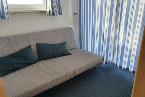 Gemütliches Wohnzimmer mit Schlafsofa und blauen Vorhängen auf einem Hausboot. Zwei Kissen.