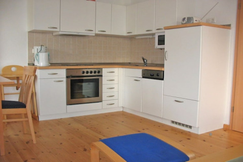 Houseboat kitchen with white cabinets, oven, stove, sink, microwave, and wooden floor and dining set.