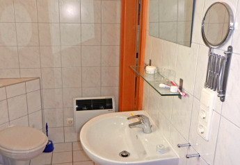 Badkamer op een woonboot met wastafel, spiegel, plankje, toilet en wandgemonteerde elektrische verwarming.