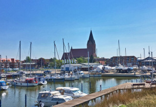 Blick von einem Hausboot auf einen ruhigen Hafen mit Segelbooten, Gebäuden und Kirche im Hintergrund.