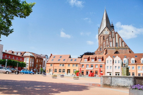 Bunte Häuser und eine große Kirche am Marktplatz unter blauem Himmel in einer deutschen Stadt.
