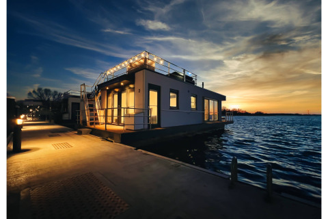 Verlichte woonboot bij zonsondergang op het water in Ribnitz-Damgarten, Duitsland, met kalme sfeer.