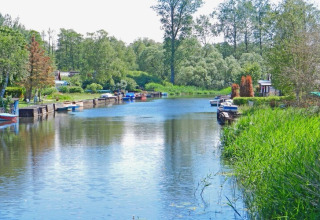 Foto van een rustige rivier met woonboten en groene natuur, genomen bij Floating House 1 in Duitsland.