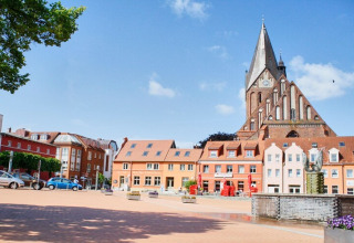 Colorful houses and a towering brick church on a bright square under blue skies in Germany.
