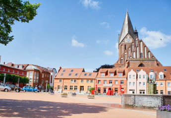 Kleurrijke huizen en een hoge bakstenen kerk op een zonnig plein in een Duitse stad.