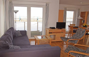 Woonkamer op een woonboot met bank, fauteuil, tv en eettafel, grote ramen met uitzicht op het water.